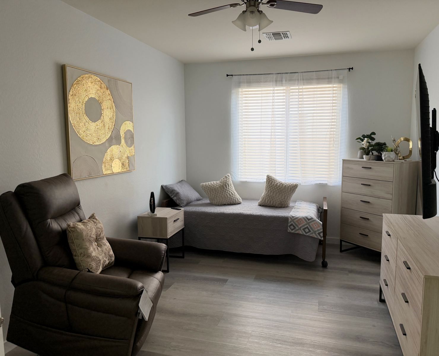 Private resident room with recliner, bed, dresser, and television
